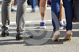 Close up of men and women legs in different shoes, high heels walking fast along the concrete road on bright sunny day. Busy lifes