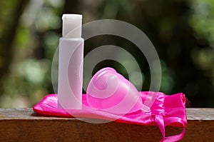 Close up of menstrual cup with cotton bag with a white flask of cream, in a blurred background