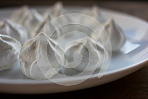 Close-up of meringue on a white plate. Marshmallows on wooden table background