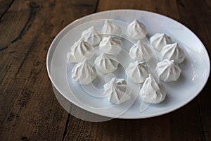 Close-up of meringue on a white plate. Marshmallows on wooden table background