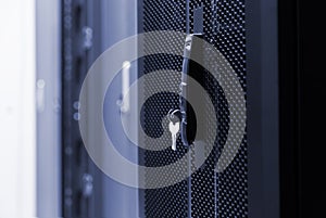 Close up meshed door with key in lock. Button in server room. Blur background of racks rows with network and hardware in the data