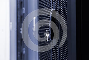 Close up meshed door with key in lock. Button in server room. Blur background of racks rows with network and hardware in the data photo
