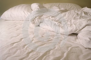 Close up messy white pillows and blanket on double bed in bedroom of resort when people wake up in morning