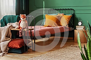 Close-up of a frame bed for a child with orange pillows standing against green wall in bright bedroom interior. Real photo