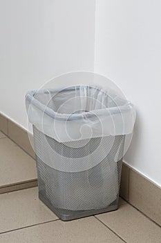 Close up of metal gray trash can with white garbage bag inside.