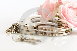 Close-up of metal handcuffs, keys and romantic pink flower
