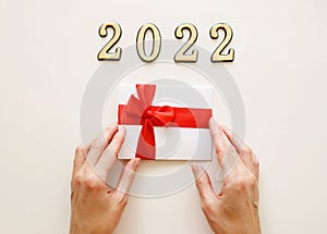 Close-up of metal numbers 2022 and hand on white background holding gift certificate discount voucher. Christmas and New Year