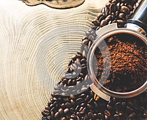 Close up of metal portafilter filled with coffee powder and coffee beans around on wooden table