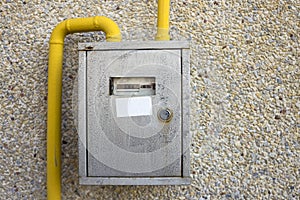 Close-up of metal steel gas meter box with connecting yellow pipes hanging on exterior light stone house wall. Construction,