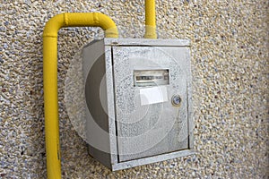 Close-up of metal steel gas meter box with connecting yellow pipes hanging on exterior light stone house wall. Construction,