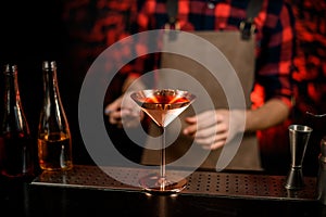 Close-up of metallic martini glass with cocktail stands at bar counter.