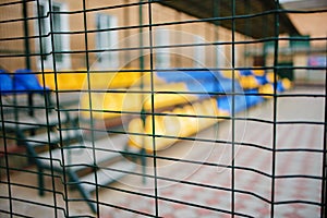 Close up metallic net-shaped fence from wire on a background of empty blue and yellow sports seats of the grand stand