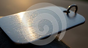 A close-up of a metallic rectangular tag with rounded edges, featuring a brushed