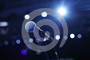 Close up of microphone in concert hall or conference room with cold lights in background.