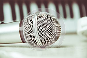 Close up on a microphone during recording session with a singer, piano in the background, music studio.