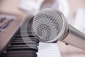 Close up on a microphone during recording session with a singer, piano in the background, music studio.