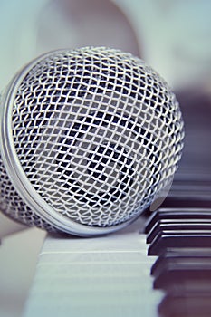 Close up on a microphone during recording session with a singer, piano in the background, music studio.