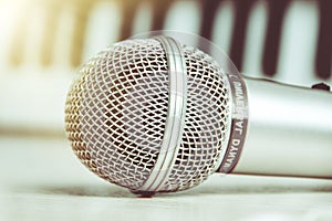 Close up on a microphone during recording session with a singer, piano in the background, music studio.