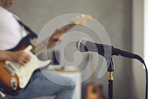 Close up of microphone in recording studio with man playing electric guitar in background