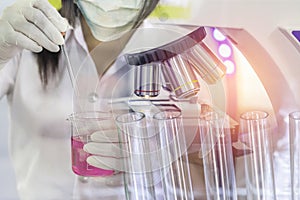 Close up microscope equipment for research experiments with scientist hand holding flask with liquid and glass test tubes