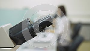 Close-up of the microscope eyepieces, on the background of a working woman lab assistant in a lab coat.