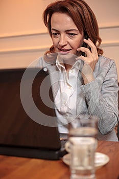 Close-up of a mid adult business woman using laptop and talking on the phone in cafe