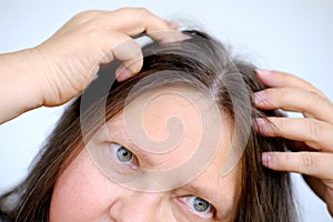 close up middle-aged female face, woman 45-50 years old looks gray hair, carefully examines hair, Aging with grace and confidence