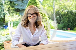 Close-up of middle aged woman wearing glasses and white shirt while relaxing on the patio at home