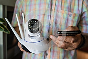 Close up on midsection of unknown man holding home security surveillance camera and mobile phone trying to install an app front