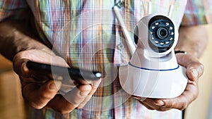 Close up on midsection of unknown man holding home security surveillance camera and mobile phone trying to install an app front