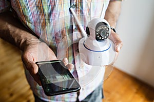 Close up on midsection of unknown man holding home security surveillance camera and mobile phone trying to install an app top view