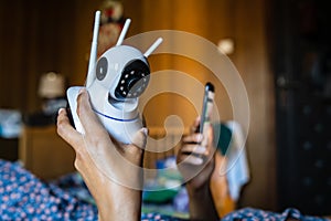 Close up on midsection of unknown woman holding home security surveillance camera and mobile phone trying to install an app while