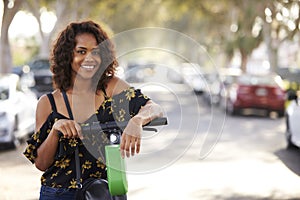 Close up of millennial African American  woman leaning on an electric scooter in the street, smiling to camera