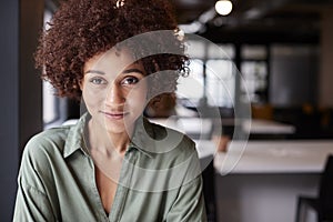 Close up of millennial black female creative sitting in an open plan office smiling to camera