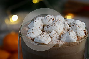 close up of mini marshmallows on hot chocolate in a glass mug, blurred lights background