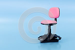 Close-up of a miniature pink office chair with a USB flash drive inserted into its base on a solid blue background