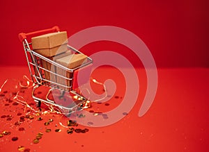 Close up of miniature shopping cart with craftpaper gift on a red background