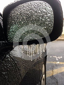 Close-up of mirror on vehicle covered in dripping freezing rain