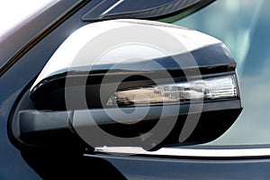 Close-up of the mirror wing of a modern black car with turn light glass.