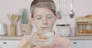 Close-up of mischievous little boy smelling milk in glass with dissatisfied facial expression. Portrait of cute