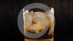 Close-up of misted glass of whiskey with ice slowly rotates on a dark background