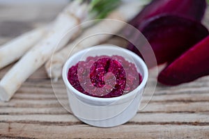 Close up mix spicy horseradish and beetroot saucer in a small glass on a rustic wooden table. Organic food