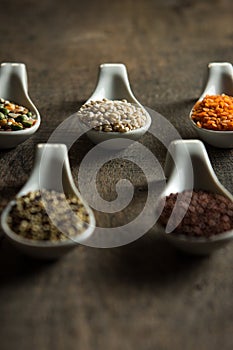 Close up of mixed grains in white spoons on wood