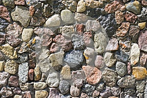 Close up of mixed pebbles texture. Pebble stones stacked into a wall on a sunny day