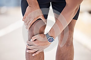 Close up of a mixed race man using his hands to hold his knee while suffering from a sports injury while running on a