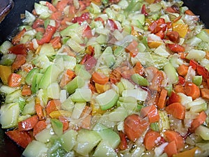 close up of a mixture of chopped vegetables frying in olive oil in a frying pan, zucchini, carrot, leek and peppers, selective