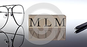 Close-up Of MLM Multi-Level Marketing Wooden Blocks on the black background with glasses and pen