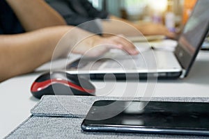 Close up mobile phone on desk with workers typing on laptop keyboard. Focus on cell phone with blurred worker in background