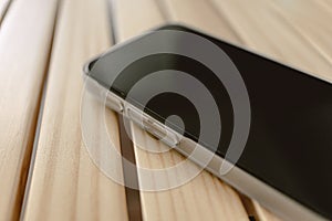 Close up of mobile phone wears white matte case left on wooden table.