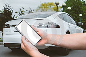 Close-up, Mockup of a smartphone in the hands of a man. Against the background of a white electric car in the city